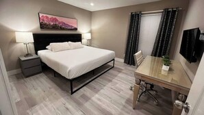 Une chambre d’hôtel comprenant un lit, une table de chevet, une lampe, un tableau au mur, une fenêtre avec des rideaux et un téléviseur.