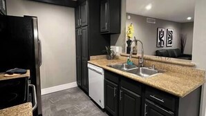 Une cuisine moderne avec des meubles de couleur sombre, un plan de travail en granit et un lave-vaisselle encastré.