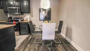 Een moderne keuken met zwarte kastjes, een roestvrijstalen magnetron en een eethoek met een witte tafel en zwarte stoelen.