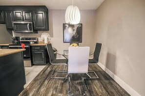 A modern kitchen with black cabinets, a stainless steel microwave, and a dining area with a white table and black chairs. - Sundance Suite 2B/2B Central (Las Vegas)