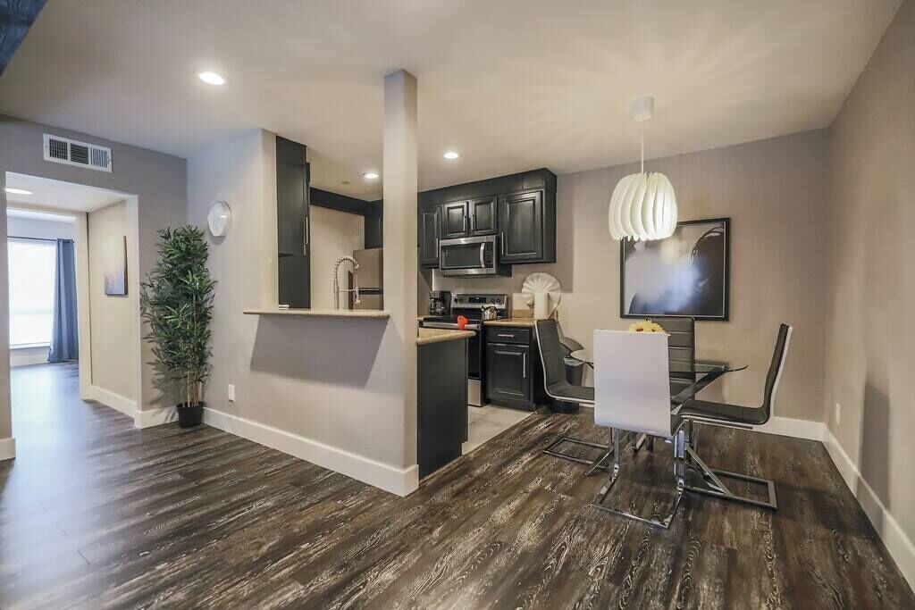 Une cuisine moderne avec un plancher en bois foncé, un coin repas avec une table et des chaises blanches, et un luminaire suspendu.