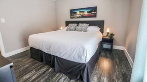 Een hotelkamer met een groot bed, een nachtkastje met een lamp en een schilderij aan de muur.