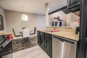 A modern kitchen with a dishwasher, a granite countertop, and a dining area with a white table and chairs. - Sundance Suite 2B/2B Central (Las Vegas)