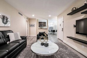A modern living room with a black leather sofa, a marble coffee table, and a flat-screen TV mounted on the wall. - Dalia Suite 2b/1b Near UNLV (Las Vegas)