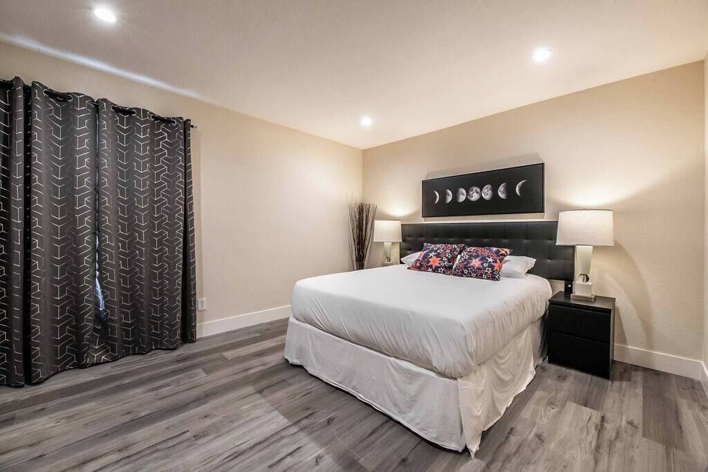 Un dormitorio con cama, mesitas de noche, una obra de arte en la pared y cortina estampada.