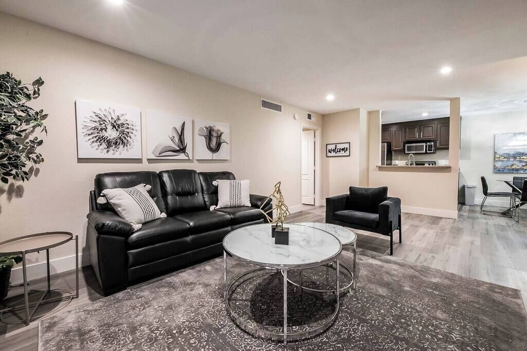 Un salon moderne avec un canapé en cuir noir, une table basse en verre et un tapis à motifs.