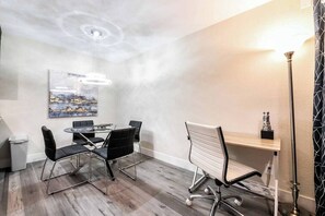 Ein Konferenzraum mit rundem Tisch, vier Stühlen, einer Whiteboard-Tafel und einem Gemälde an der Wand.