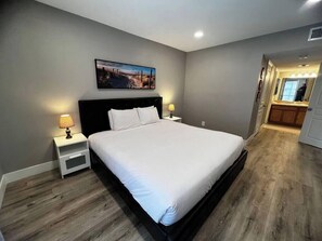 Une chambre à coucher avec un grand lit, deux tables de chevet avec des lampes, un tableau au mur et un plancher en bois.