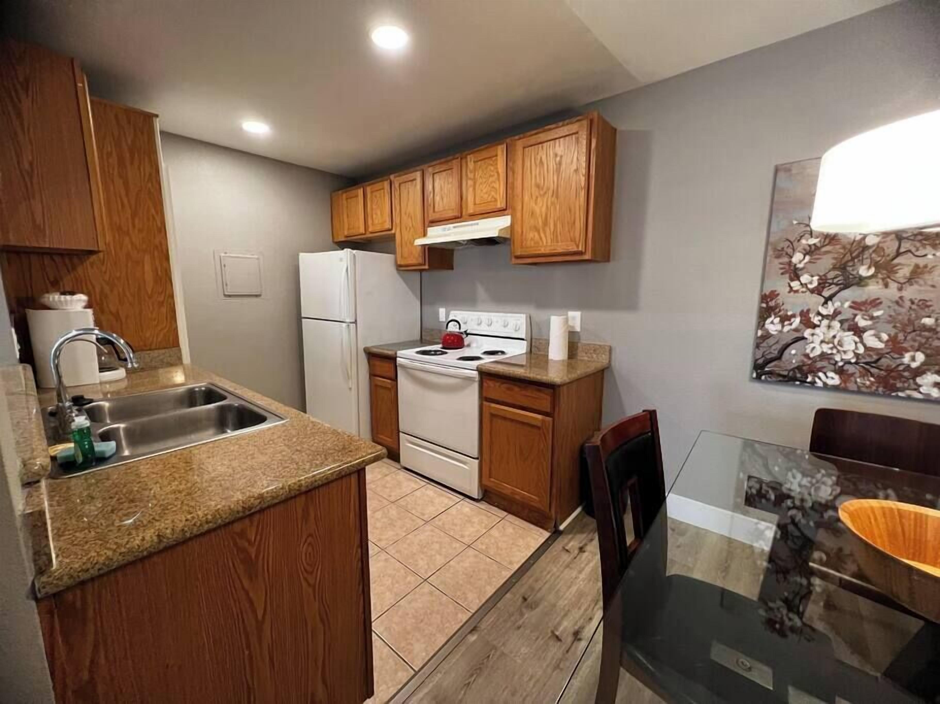 Una cocina funcional con armarios de madera, un refrigerador blanco, una estufa y una zona de comedor con una mesa de vidrio.