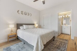 Une chambre à coucher comprenant un lit, des tables de chevet, une commode, un miroir et une porte donnant sur une salle de bain.