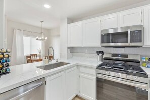 A kitchen with white cabinets, a stainless steel stove, and a double microwave. - Belmont Suite Modern 2 /2 condo (Las Vegas)