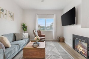 A living room with a sofa, coffee table, TV, fireplace, and a window with a view. - Belmont Suite Modern 2 /2 condo (Las Vegas)