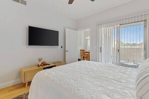 A bedroom with a bed, a TV mounted on the wall, a wooden dresser, and a sliding glass door leading to an outdoor area. - Belmont Suite Modern 2 /2 condo (Las Vegas)