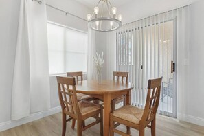 Un coin repas avec une table ronde en bois et six chaises, un lustre et une vue à travers une porte vitrée.
