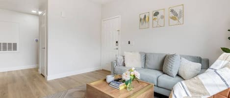 Un salon moderne avec un canapé gris clair, une table basse en bois ornée de livres et d’un vase de fleurs, et un tapis à motifs.