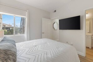 Een slaapkamer met een bed, een aan de muur bevestigde televisie en een raam met gordijnen.
