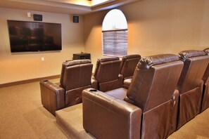 A home theater with leather reclining chairs, a large flat-screen TV, and a window with blinds. - Huntley Suite Luxury 2b/2b condo (Las Vegas)