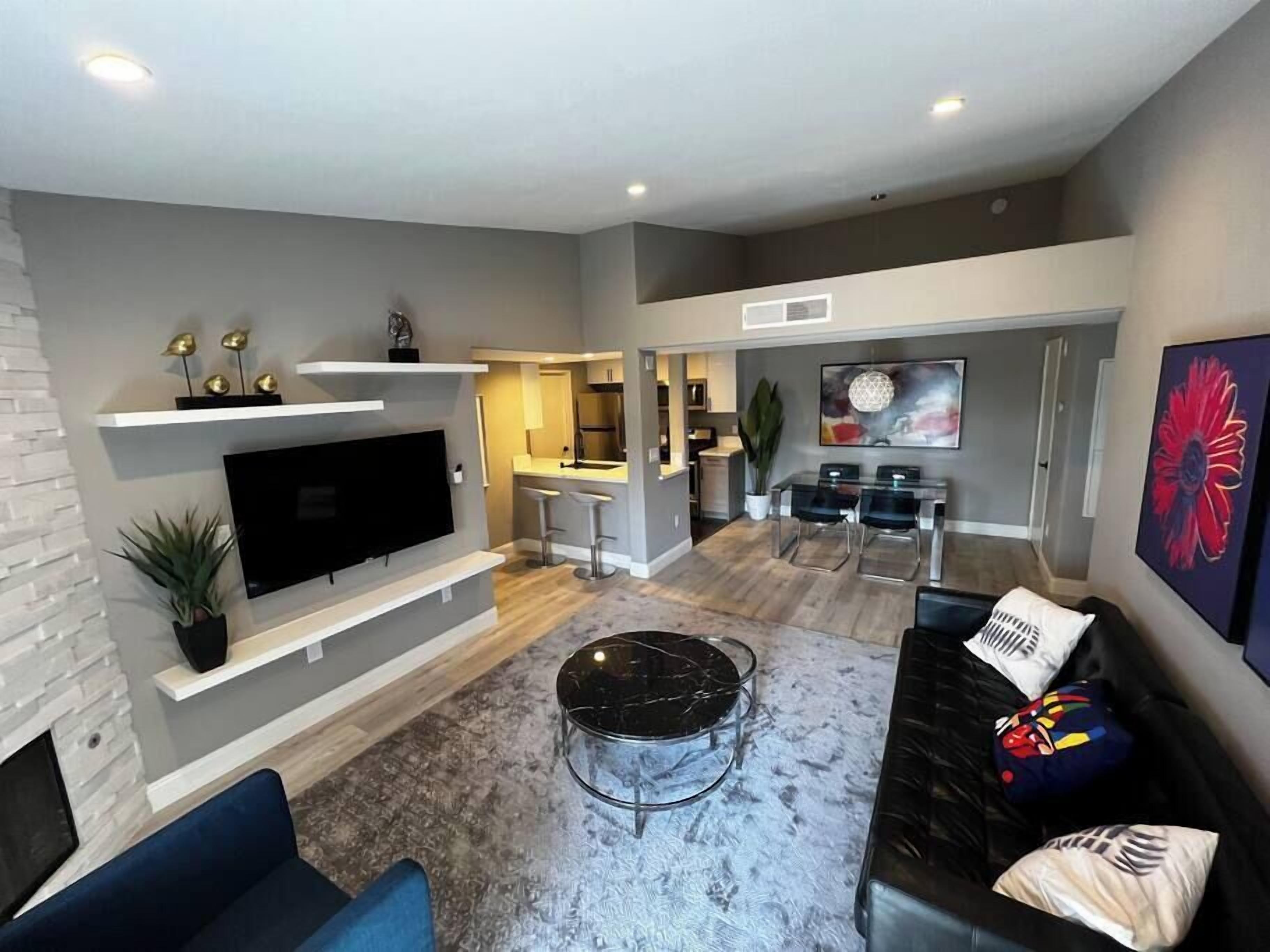 A modern living room with a flat-screen TV, a black coffee table, and a sofa with decorative pillows.