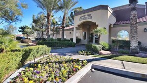 A building labeled 'RANCHO VIEJO CLUBHOUSE' with a paved entrance, surrounded by palm trees and a flower bed. - Huntley Suite Luxury 2b/2b condo (Las Vegas)