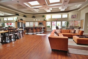 A spacious living area with a wooden floor, a large sofa set, a dining table with chairs, and a kitchen area with a refrigerator and microwave. - Huntley Suite Luxury 2b/2b condo (Las Vegas)