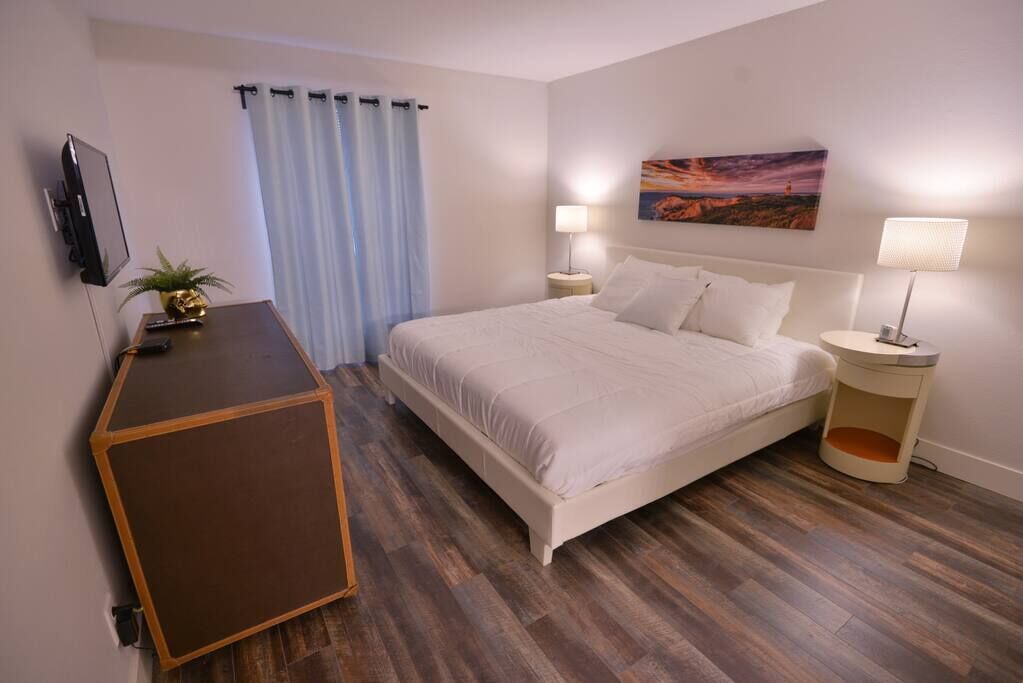 Ein Hotelzimmer mit Bett, Schreibtisch, Fernseher, einem Gemälde und einer Lampe.