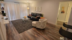 Ein stilvolles Wohnzimmer mit einer schwarzen Ledersofa, einem gemusterten Sessel und einem geometrischen Teppich.