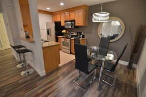 A modern kitchen with wooden cabinets, a microwave, and a dining area with a glass table and chairs. - Park Suite 1B/1B Close to strip (Las Vegas)