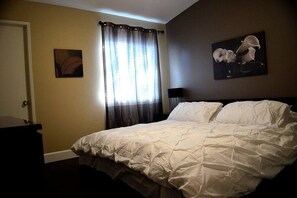 Ein Schlafzimmer mit einem Bett, einer Tür, einem Fenster mit Vorhängen und zwei an der Wand befestigten Kunstwerken.
