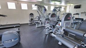 Un gimnasio con diferentes máquinas de ejercicio, una cinta de correr y un espejo grande.
