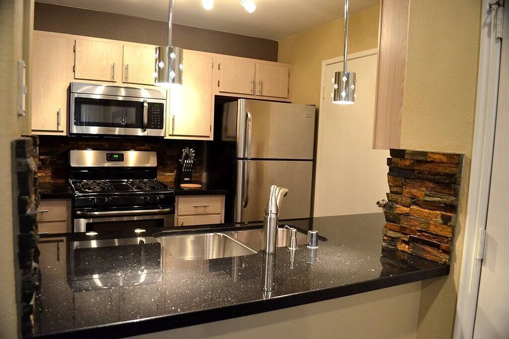 A modern kitchen with stainless steel appliances, a granite countertop, and wooden cabinetry.