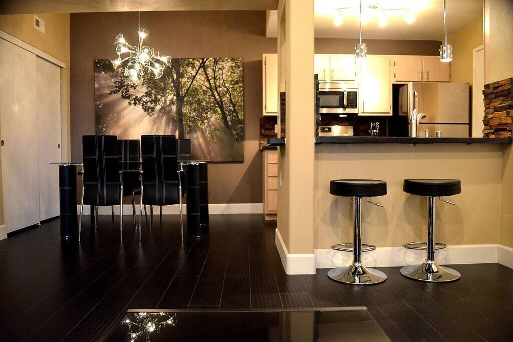 A modern kitchen with stainless steel appliances, a dining area with black chairs, and a bar stool area.