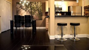 Una cocina moderna con electrodomésticos de acero inoxidable, una zona de comedor con sillas negras y una barra con taburetes.