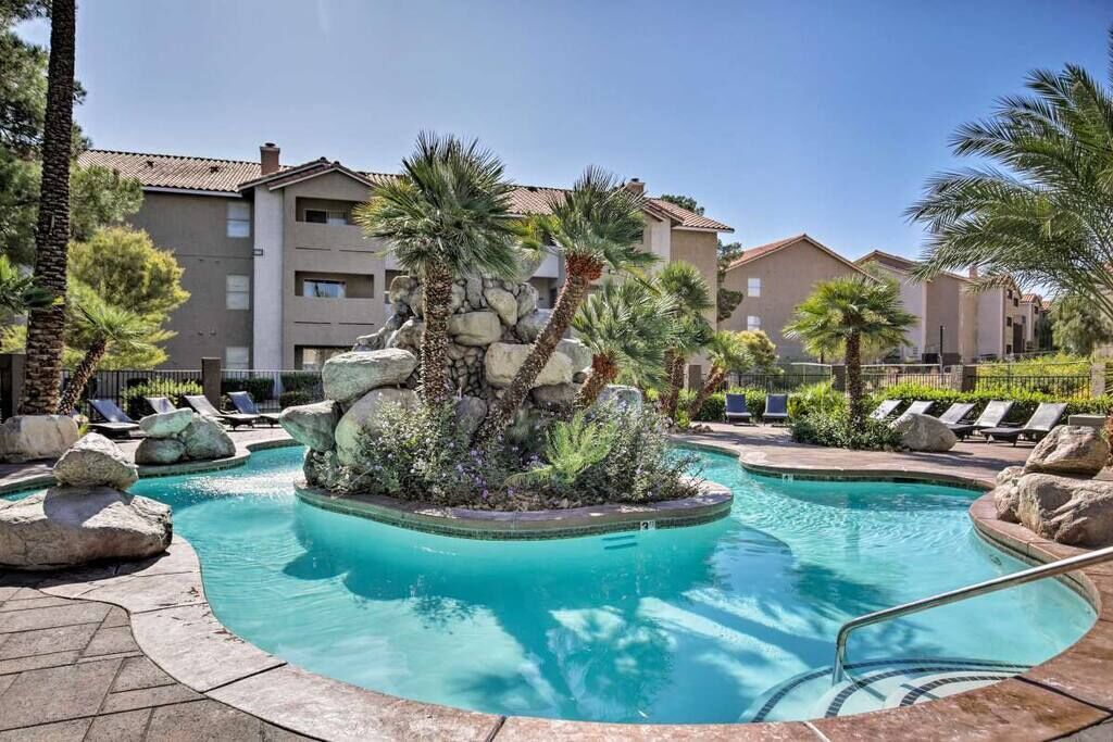 A swimming pool with a rock feature surrounded by lounge chairs and palm trees.