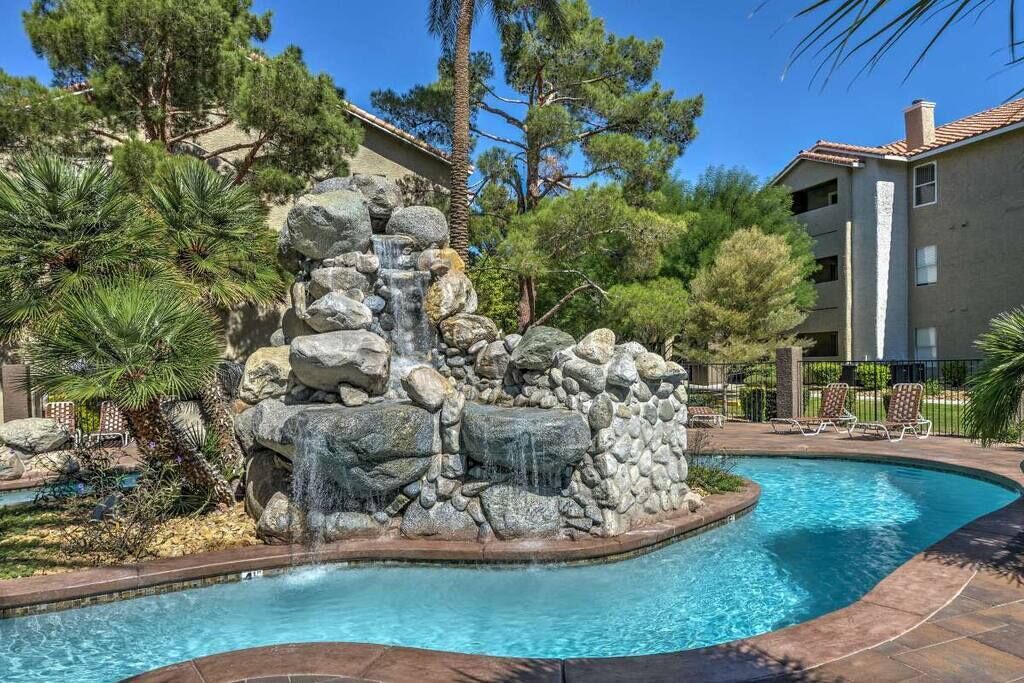 A swimming pool with a waterfall feature surrounded by rocks and pine trees.