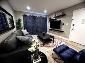A modern living room with a sofa, a coffee table, a TV, and a blue chair. - Kona Suite 1b/1b fully remodeled (Las Vegas)