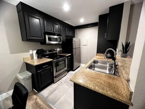 A modern kitchen with black cabinets, stainless steel appliances, and granite countertops. - Kona Suite 1b/1b fully remodeled (Las Vegas)