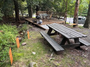 En träaltan med picknickbord och en grill, omgiven av träd.