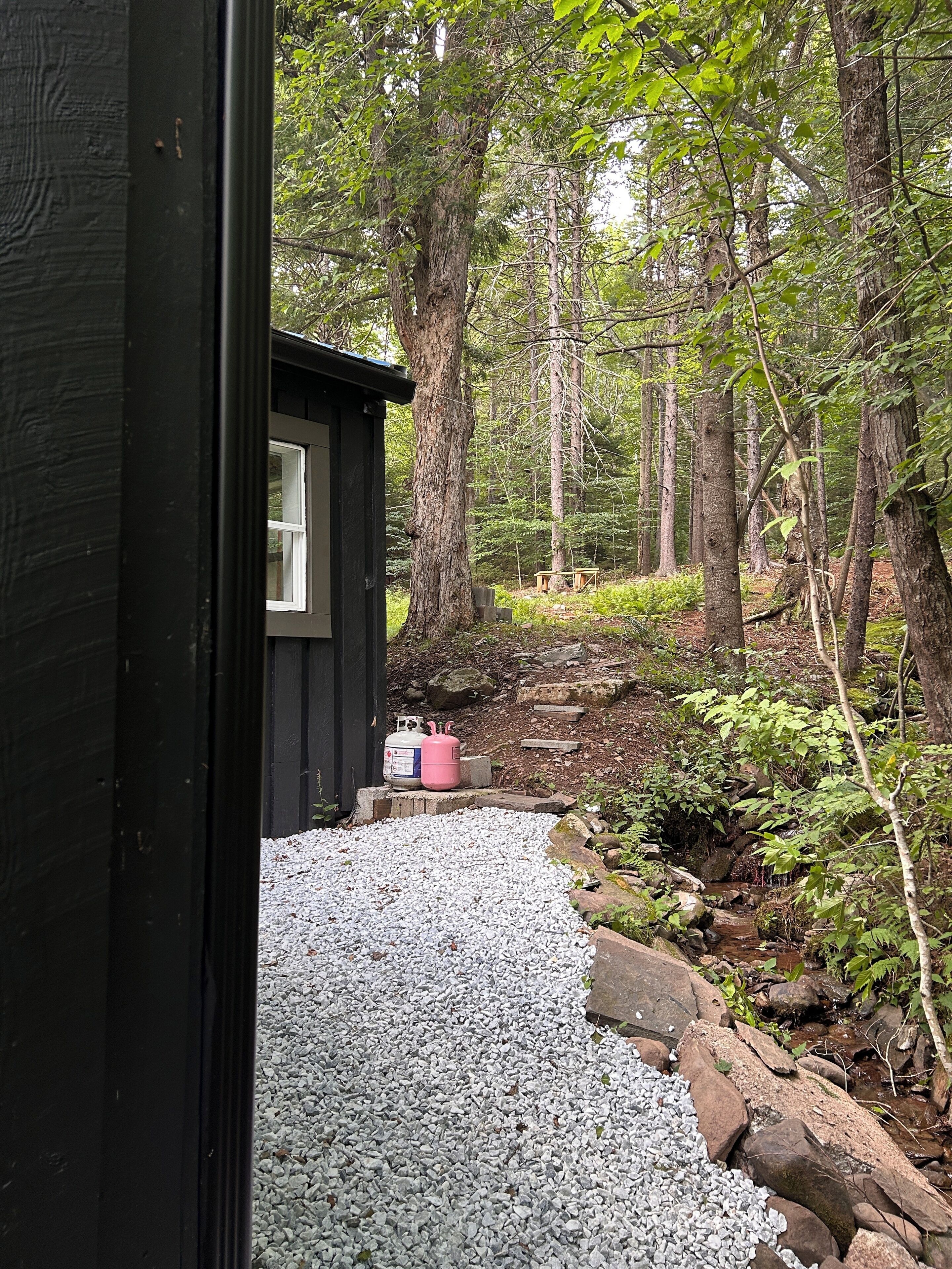 A cabin with a gravel path leading to a wooden deck, surrounded by a forest.