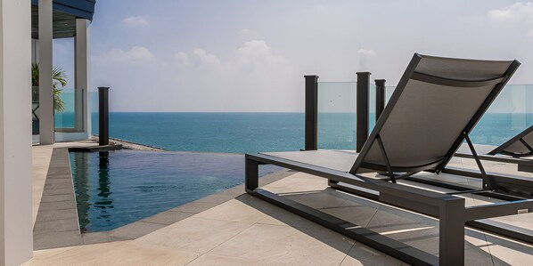 Uima-altaan reunalla on oleskelualue, jossa on aurinkotuoli, lasikaide ja näkymä merelle.