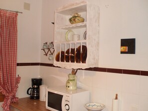 Uma cozinha com micro-ondas, cafeteira, prateleira com louças e um suporte suspenso para xícaras.