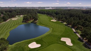An aerial view of a golf course with a large pond, sand bunkers, and surrounding trees. - Magnolia Pointe 4893-304 (Myrtle Beach)