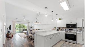 A modern kitchen with white cabinetry, a central island, and a dining area with a view to the outdoors. - Magnolia Pointe 4893-304 (Myrtle Beach)