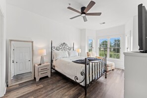 Ein Schlafzimmer mit Bett, Nachttischen, Deckenventilator, Fenster mit Blick und einer Tür.