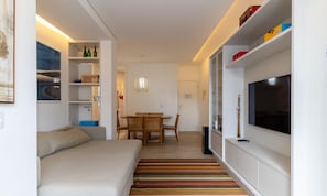 Un salon moderne comprenant un canapé, une table à manger, des chaises, un téléviseur et une bibliothèque.
