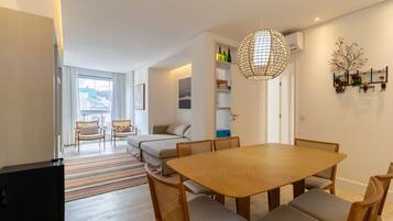 A modern living room with a dining area, a sofa, a TV, and a large window.