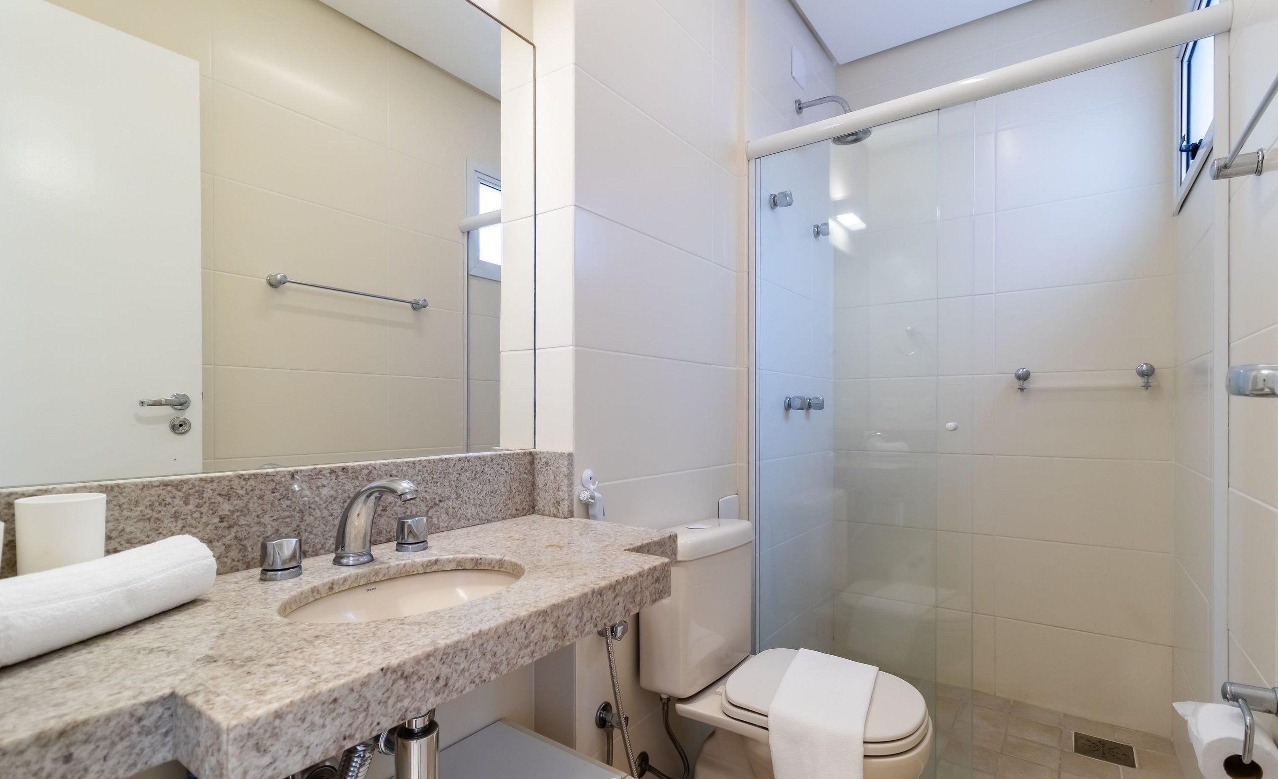 Un baño con lavamanos de mármol, inodoro, ducha con puerta de vidrio y toallero.