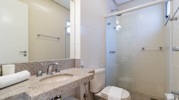 Un baño con lavamanos de mármol, inodoro, ducha con puerta de vidrio y toallero.