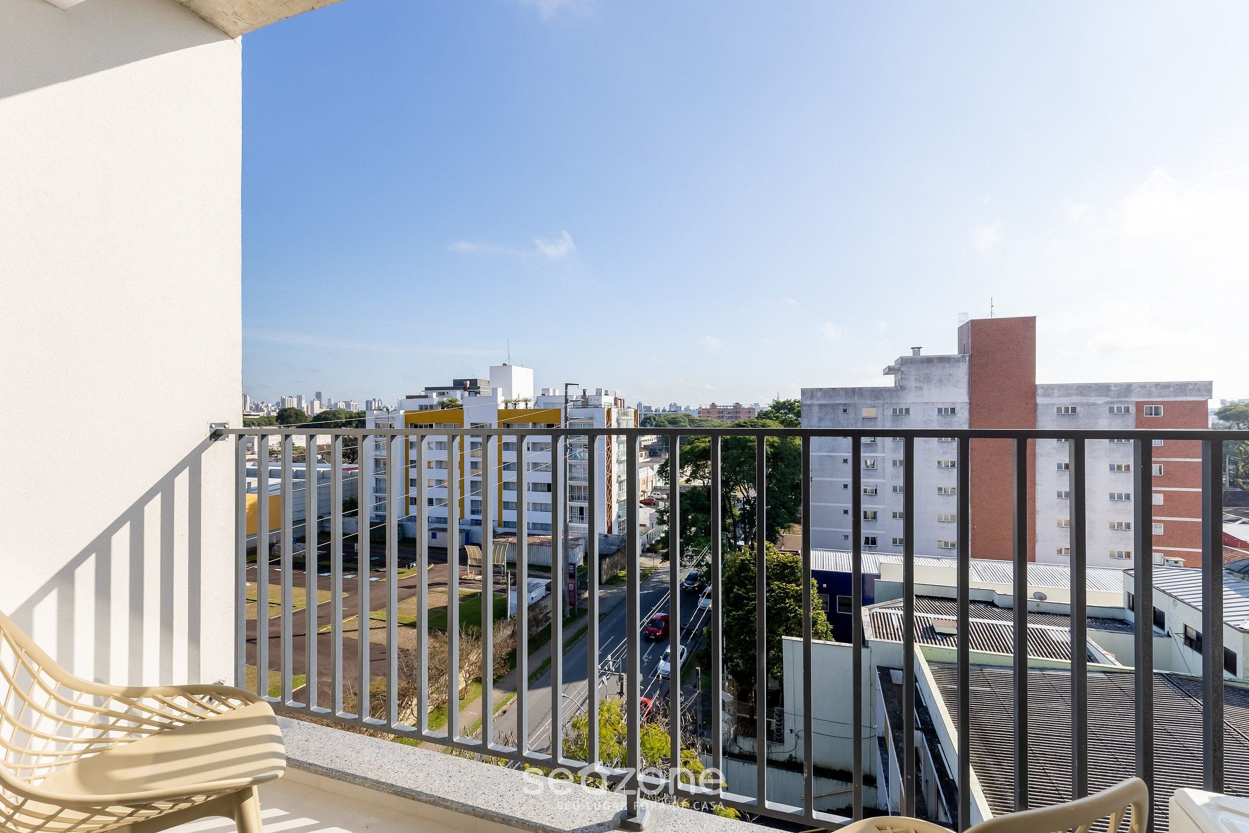 A balcony with a view of a cityscape, including buildings and a parking area.