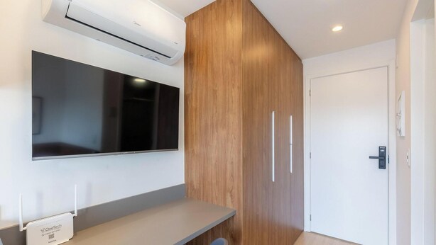 A modern room with a flat-screen TV mounted on the wall, a wooden panel wall, a white door, and a small desk with a chair.
