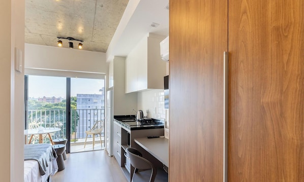 Uma cozinha moderna com uma janela ampla, uma área de jantar com mesa e cadeiras, e uma varanda com vista para a cidade.